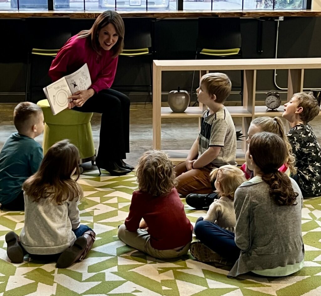 Brittany Kiser reads to a group of children that are seated on a rug.