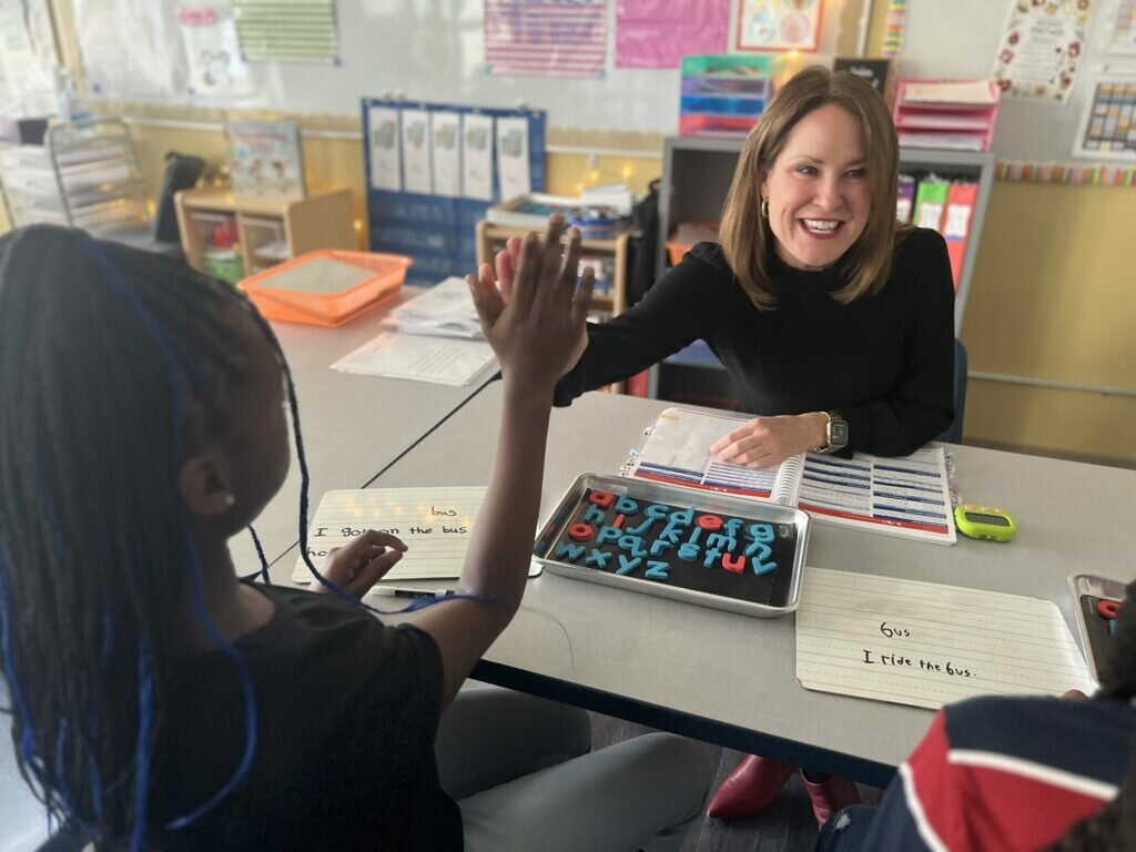 Brittany Kinser smiles and gives a student a high-five while teaching literacy in a small group.
