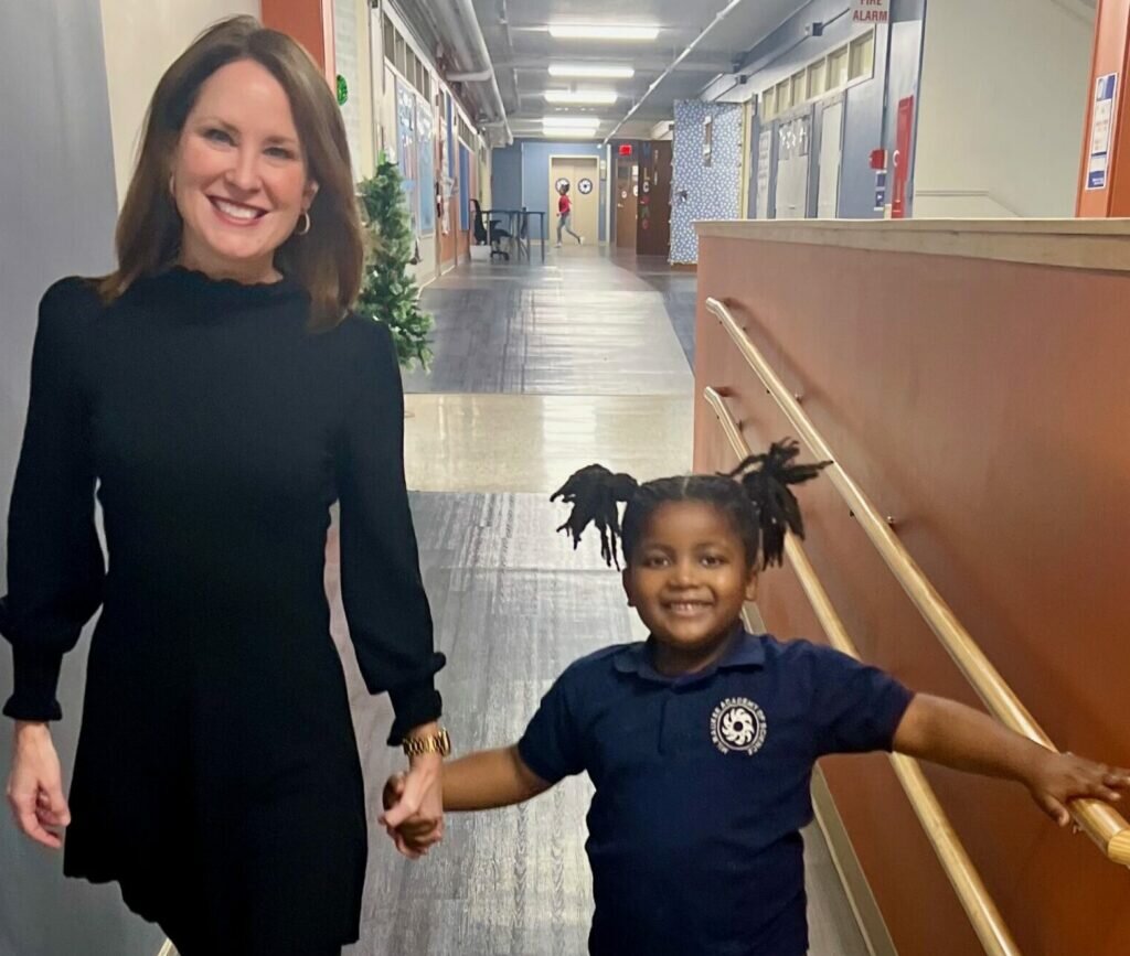 Brittany Kinser holds hands with a young student. She and the student are smiling.